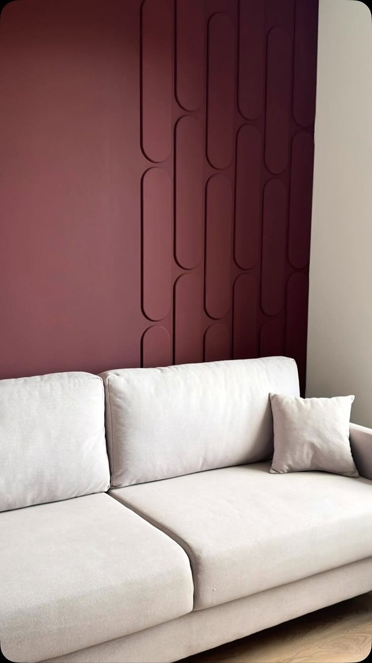 Maroon textured wall panels with vertical pill shapes behind a light grey modern sofa.