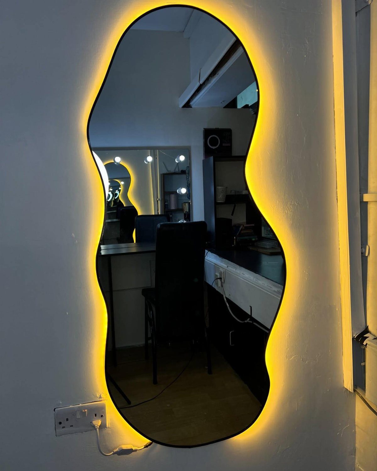 21 Bedroom Wall Decor Ideas With Photos for Every Style 20 An irregularly shaped mirror with a glowing yellow backlight mounted on a white wall.