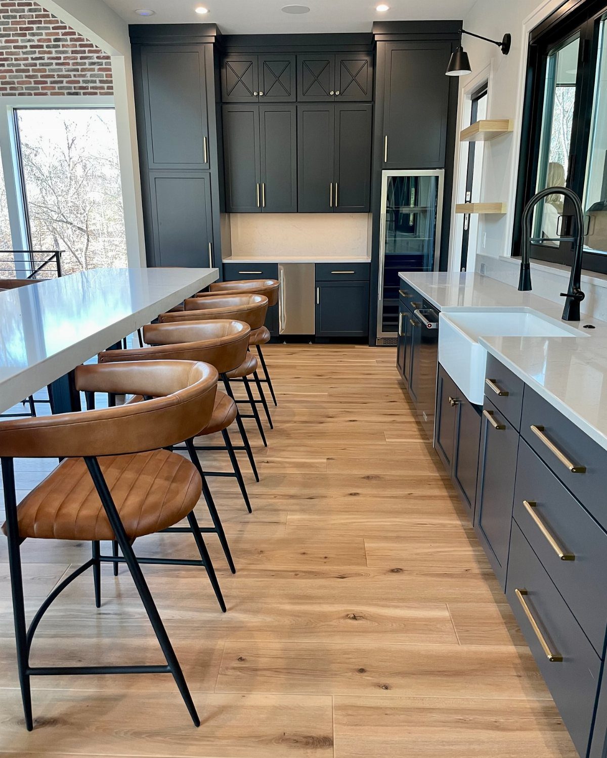 Light blonde oak wood floors in a modern kitchen with dark blue cabinets and white countertops.