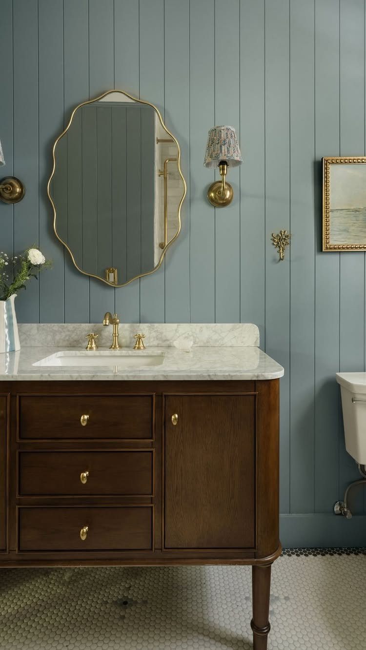 Blue-grey vertical wood panel wainscotting on a bathroom wall behind a marble vanity and gold mirror.
