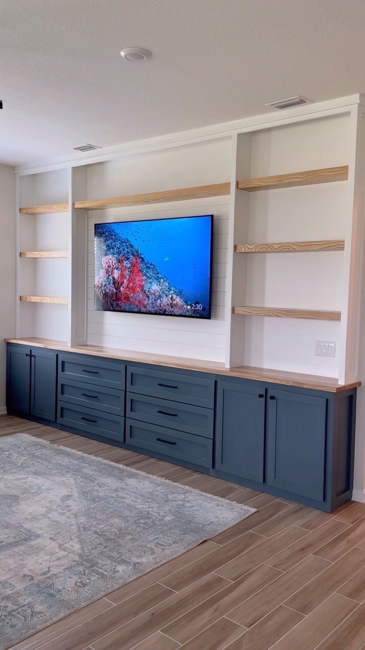 Built-in white wall unit with navy blue cabinets, wooden shelves, and a mounted television.