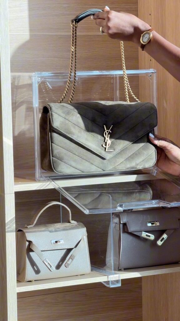 Hands reaching for designer handbags displayed on clear acrylic shelves in a wooden closet.