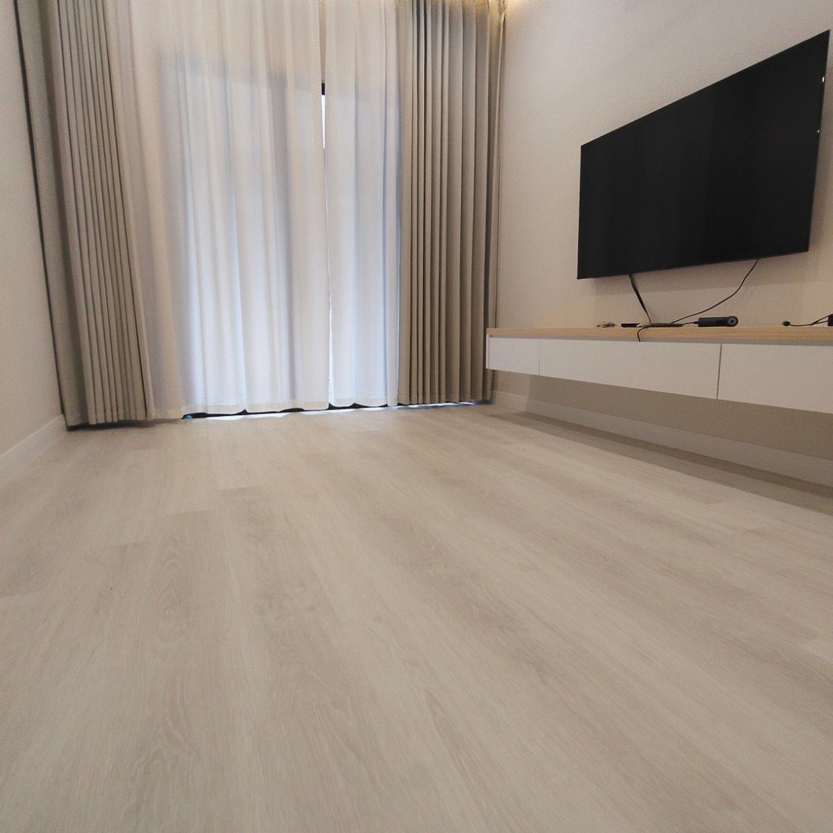 Light whitewashed wood planks covering the floor of a modern living room with white curtains.