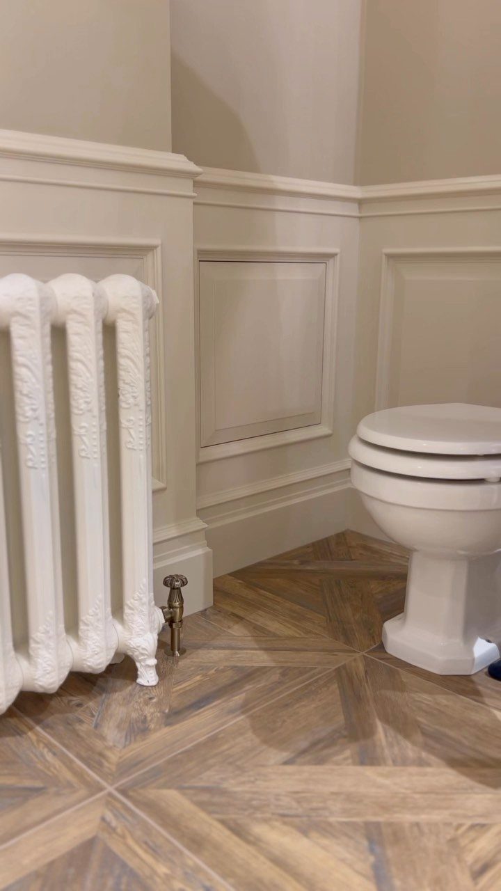 Cream wainscotting panels installed on bathroom walls above patterned wood-look tile flooring.