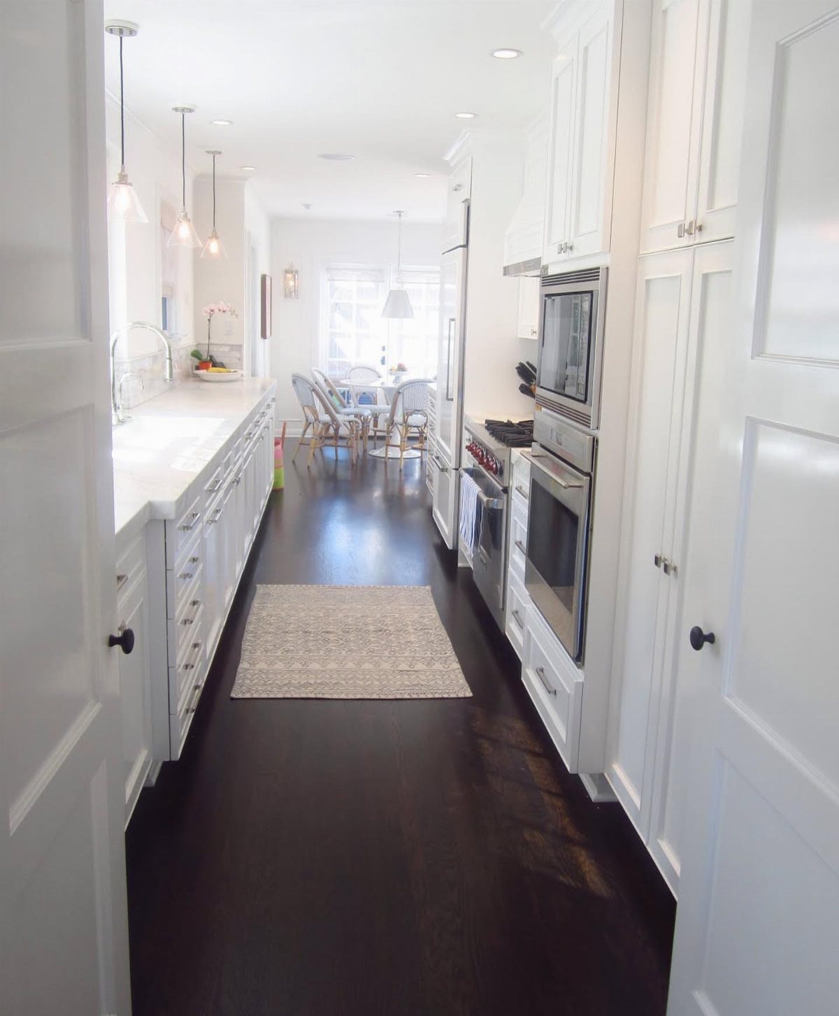 Dark Wood Floors Kitchen: 6 Looks That Balance the Floor 2 White kitchen cabinets and countertops contrasting with dark wood flooring in a long narrow room.