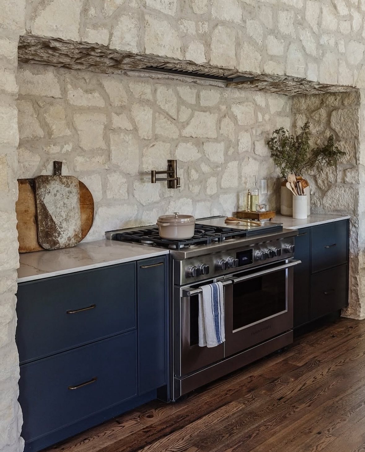 Dark Wood Floors Kitchen: 6 Looks That Balance the Floor 4 Dark wood floors in a kitchen with navy blue cabinets and a stone wall.