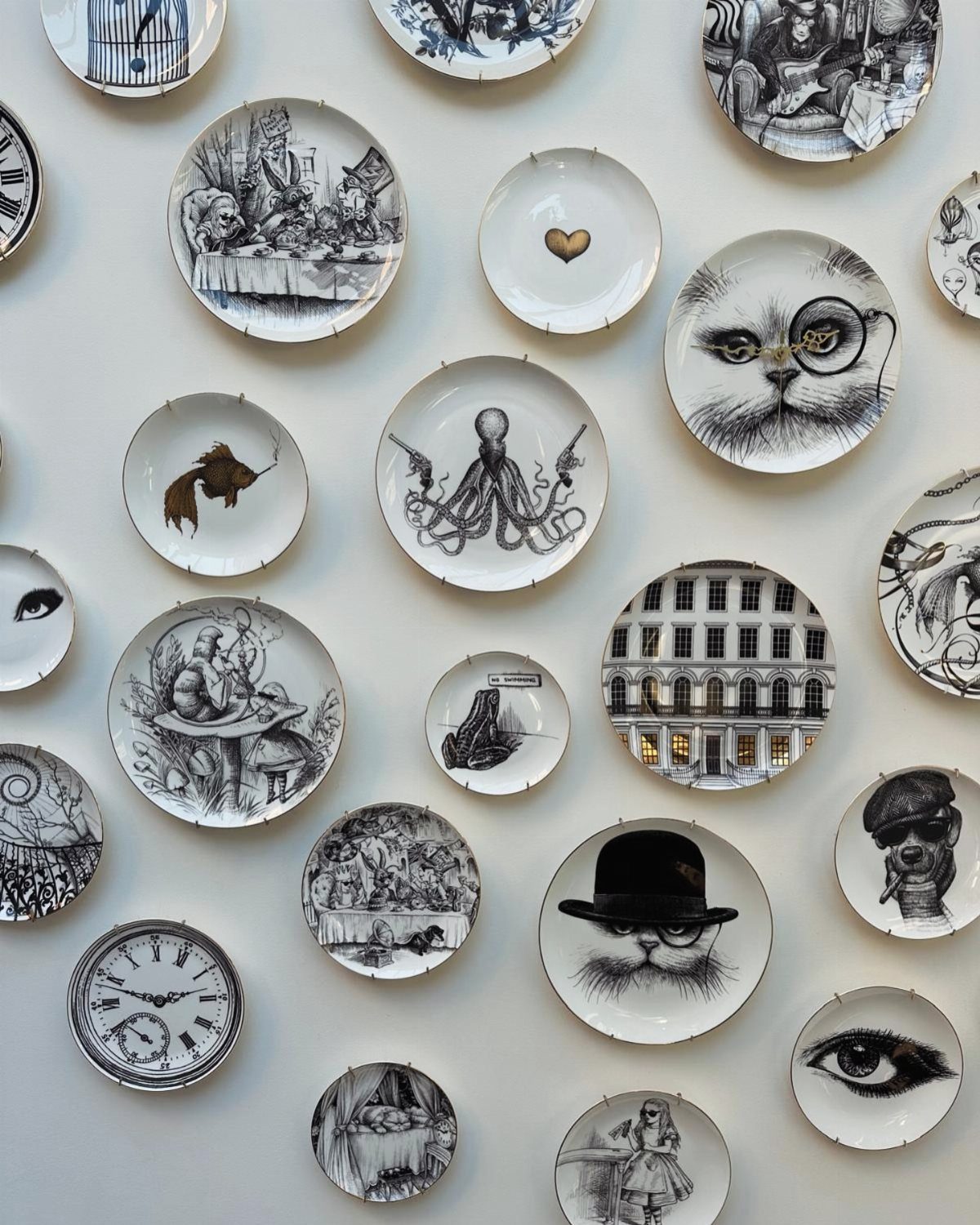 Decorative white ceramic plates with black ink illustrations mounted on a white wall.