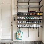 Black metal wire racks mounted on a white wall holding multiple rows of various shoes.