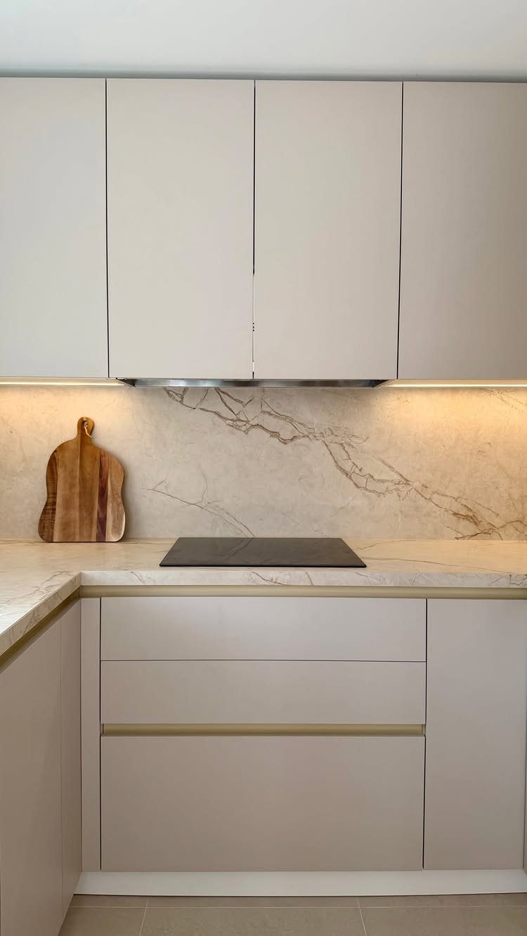 15 Kitchen Renovation Ideas for Getting the Function Back Into the Room 4 Modern kitchen with beige cabinets, marble-patterned countertops, and a matching backsplash under warm lighting.