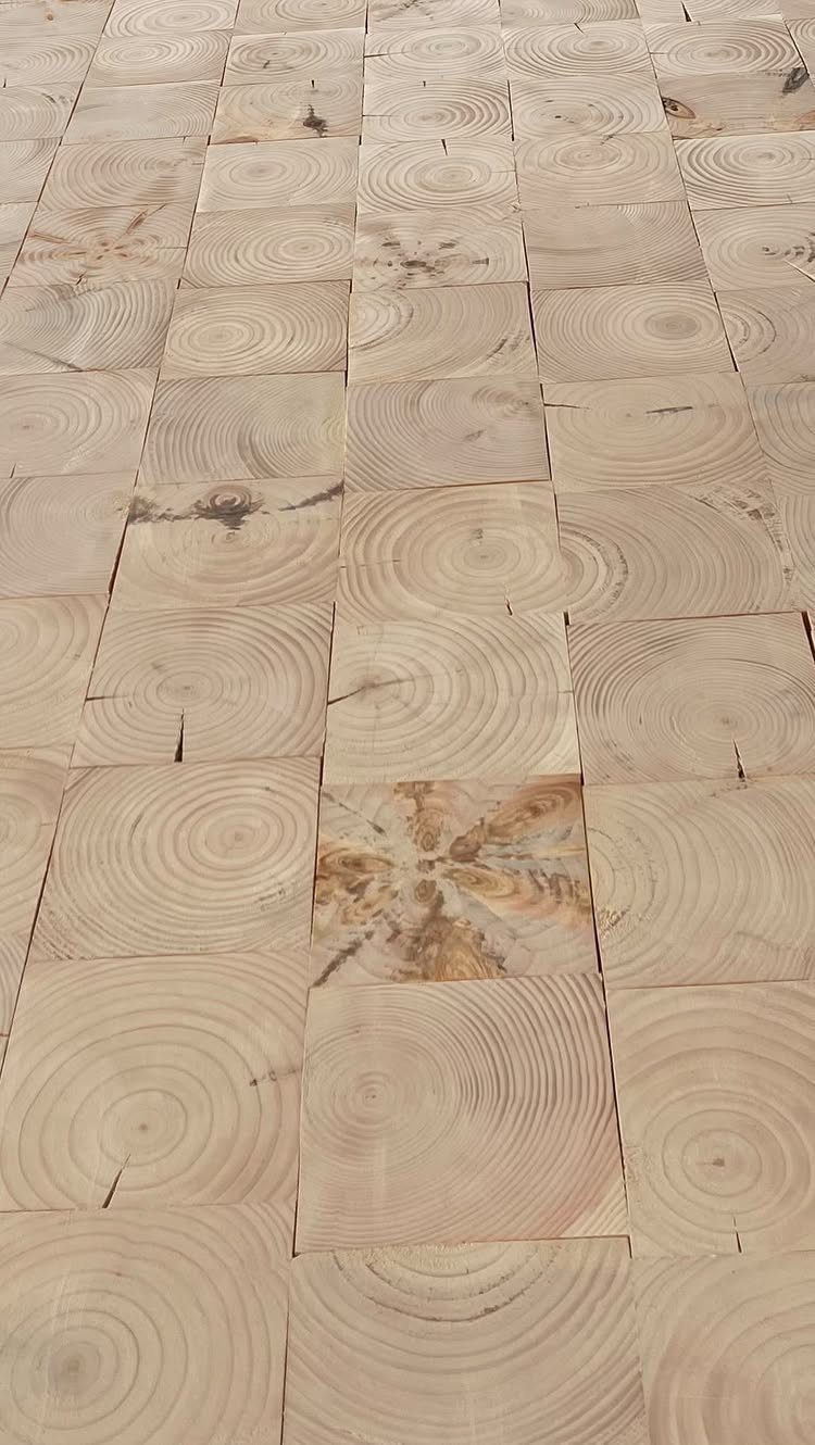 Light-colored wooden floor tiles featuring prominent natural tree ring patterns in a grid layout.