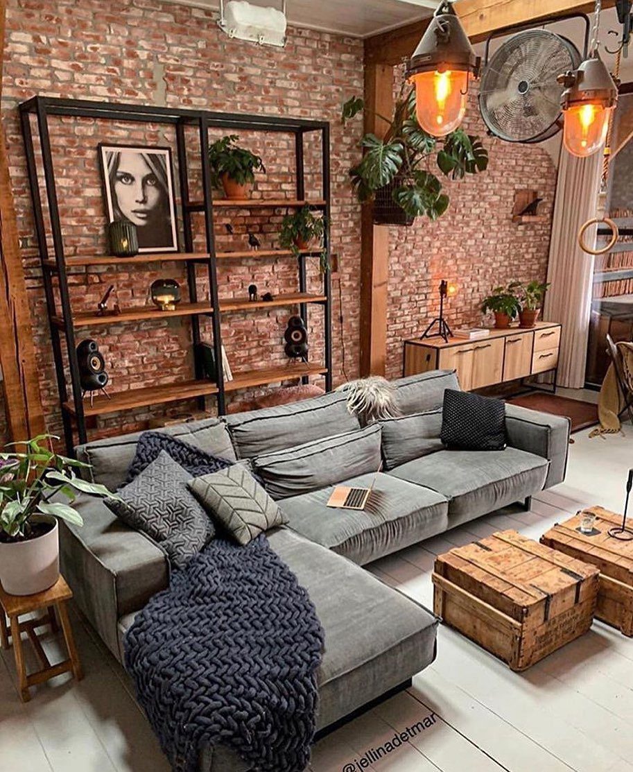 Grey sectional sofa and black shelving unit set against an exposed red brick wall.