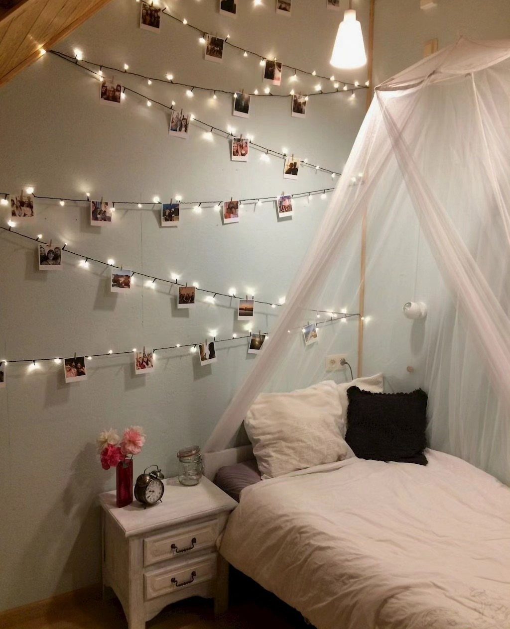 21 Bedroom Wall Decor Ideas With Photos for Every Style 3 Fairy lights with small photographs clipped to them hanging over a white bed in a bedroom.