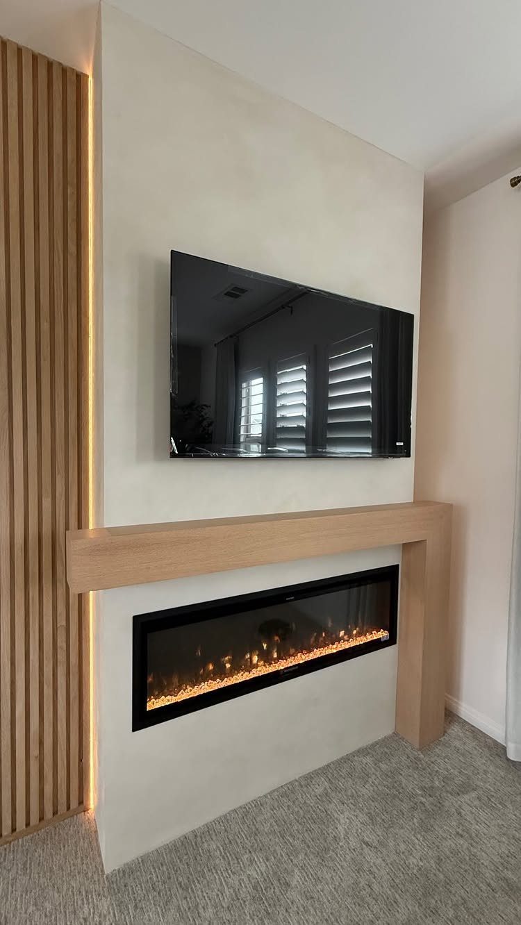 21 Bedroom Wall Decor Ideas With Photos for Every Style 12 A modern electric faux fireplace with a light wood mantel mounted on a white wall.