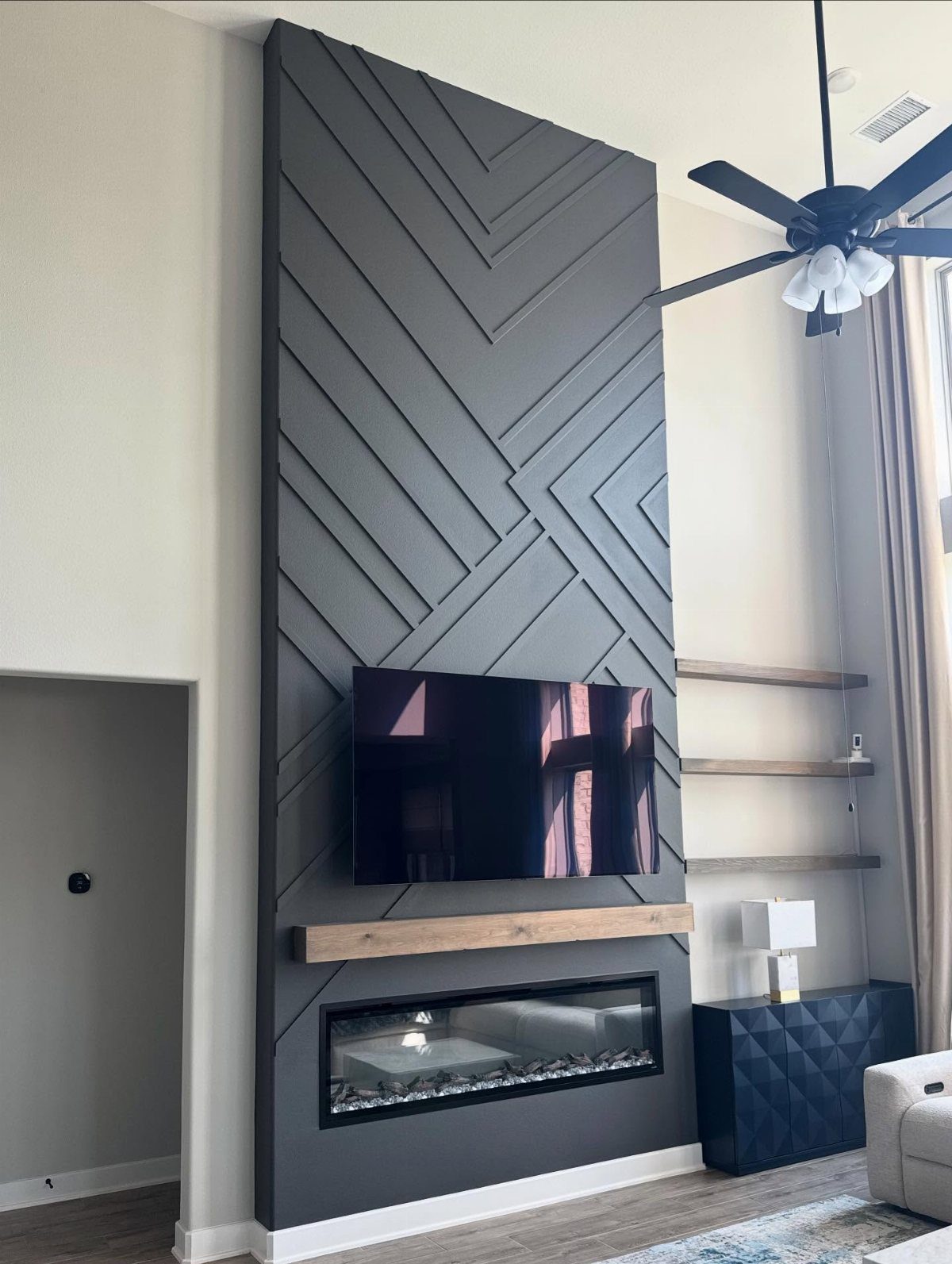 Geometric dark grey accent wall with a mounted television and a modern linear fireplace below.