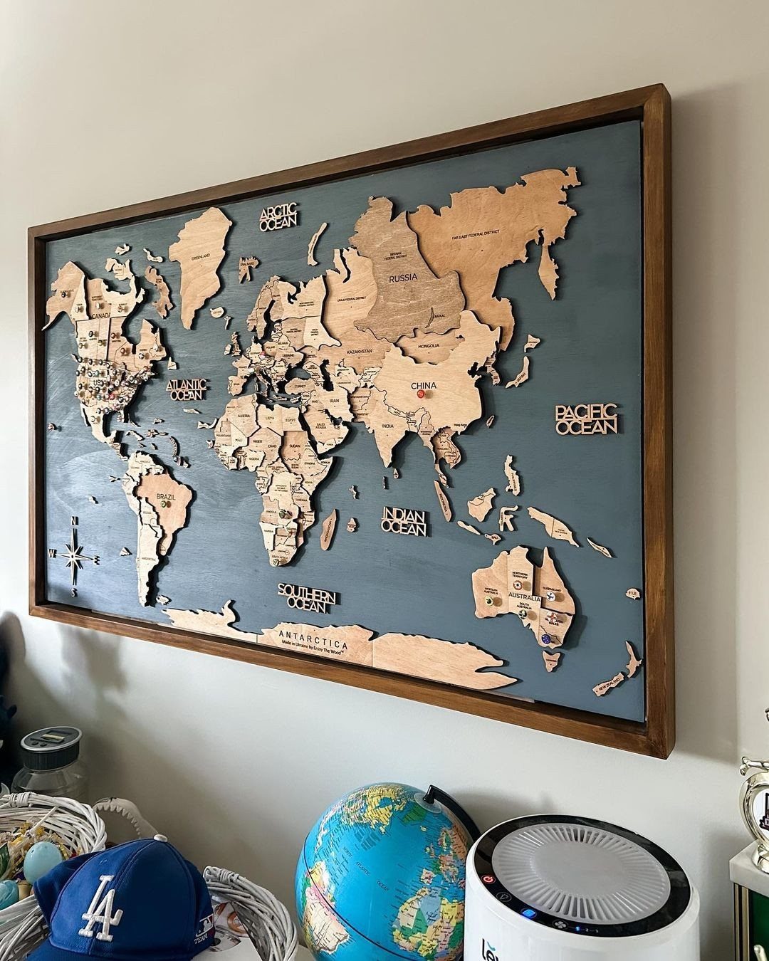 21 Bedroom Wall Decor Ideas With Photos for Every Style 4 A large wooden 3D world map in a dark frame hanging on a white wall.