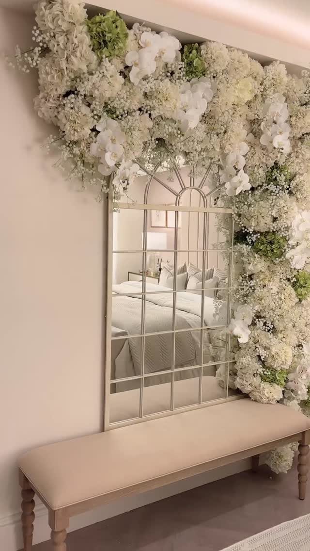 21 Bedroom Wall Decor Ideas With Photos for Every Style 14 White and green fresh flowers framing a large arched window-pane mirror above a beige bench.