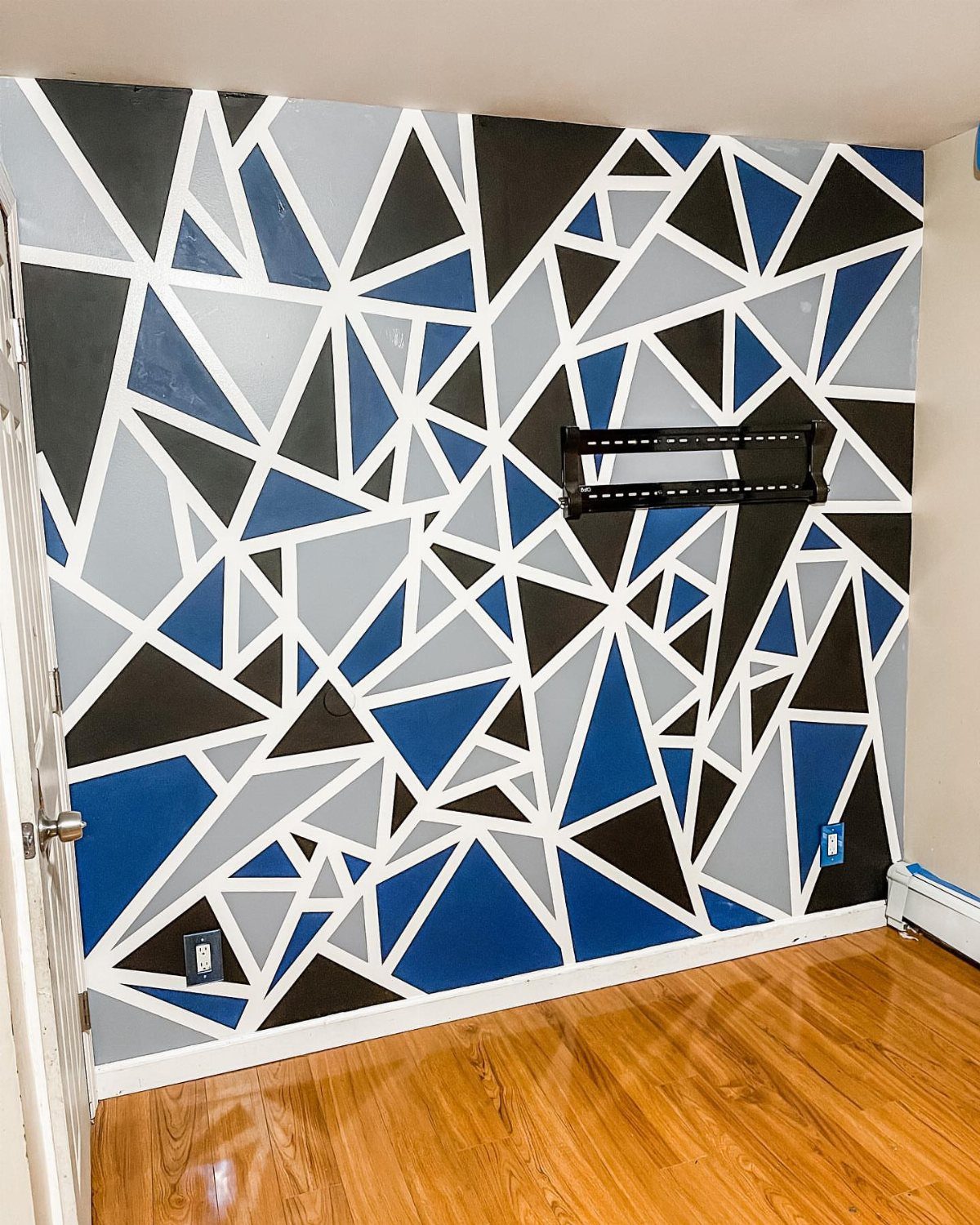 20 Bedroom Wall Designs for Accent, Texture and Art 13 A bedroom wall decorated with a large blue, gray, and black geometric painted pattern.