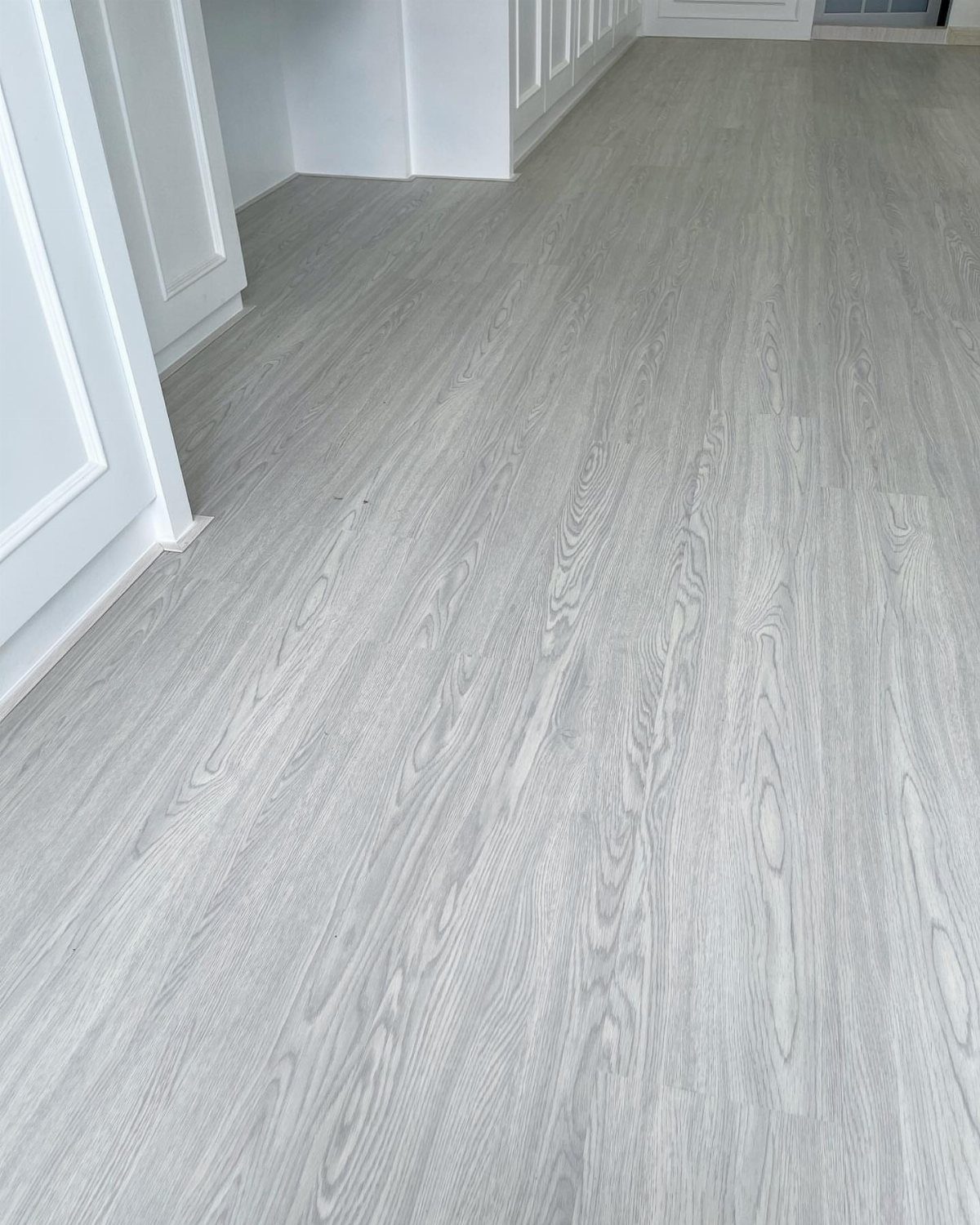 Light gray wood-textured vinyl flooring planks installed in a bright room with white walls.