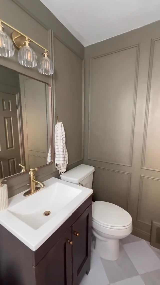 Grey paneled wainscoting in a bathroom with a white toilet and dark vanity.