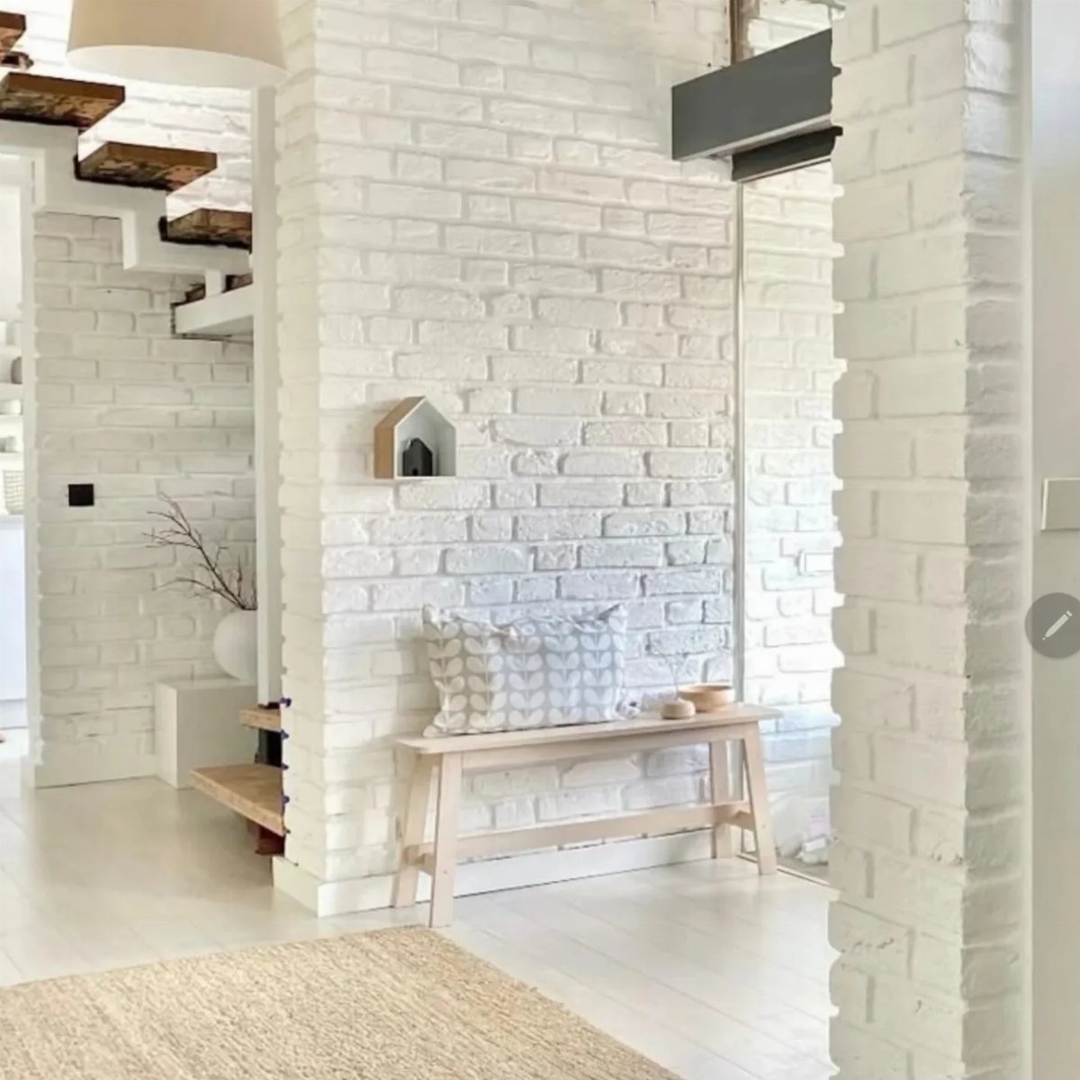 White painted brick wall in a bright room with a wooden bench and staircase.