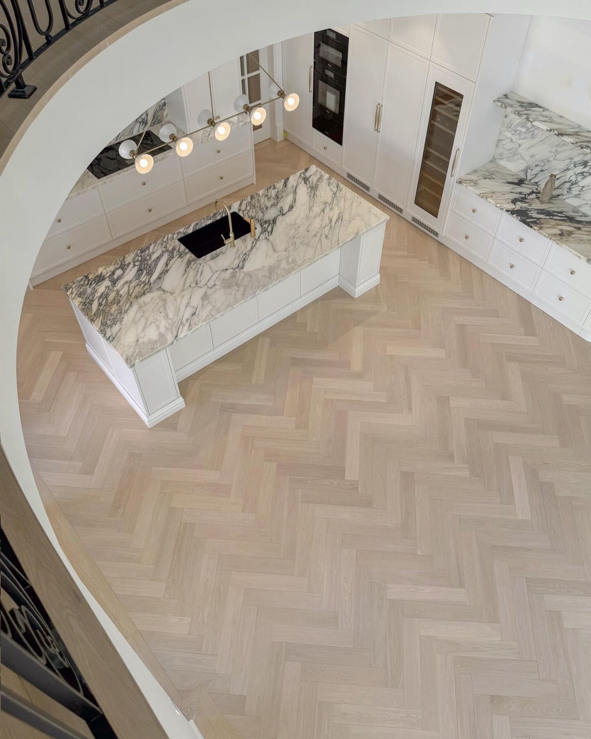 Light wood herringbone pattern flooring in a modern white kitchen with a marble island.