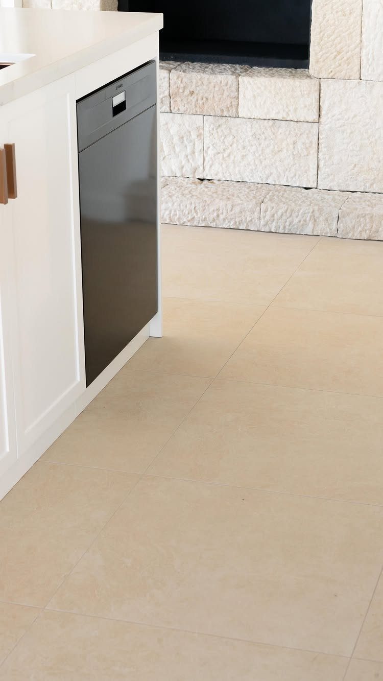 Kitchen Floor Tiles Design: 13 Ideas for Stone, Ceramic & Patterned Floors 9 Light beige stone tiles covering a kitchen floor next to white cabinetry and a stone wall.