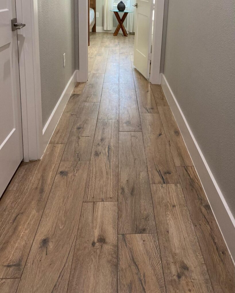 Light brown wood plank flooring extending through a narrow hallway with grey walls.