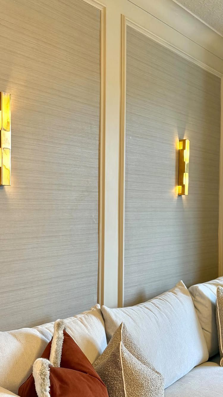 Textured grey wallpapered wall with gold sconces and white molding above a sofa.