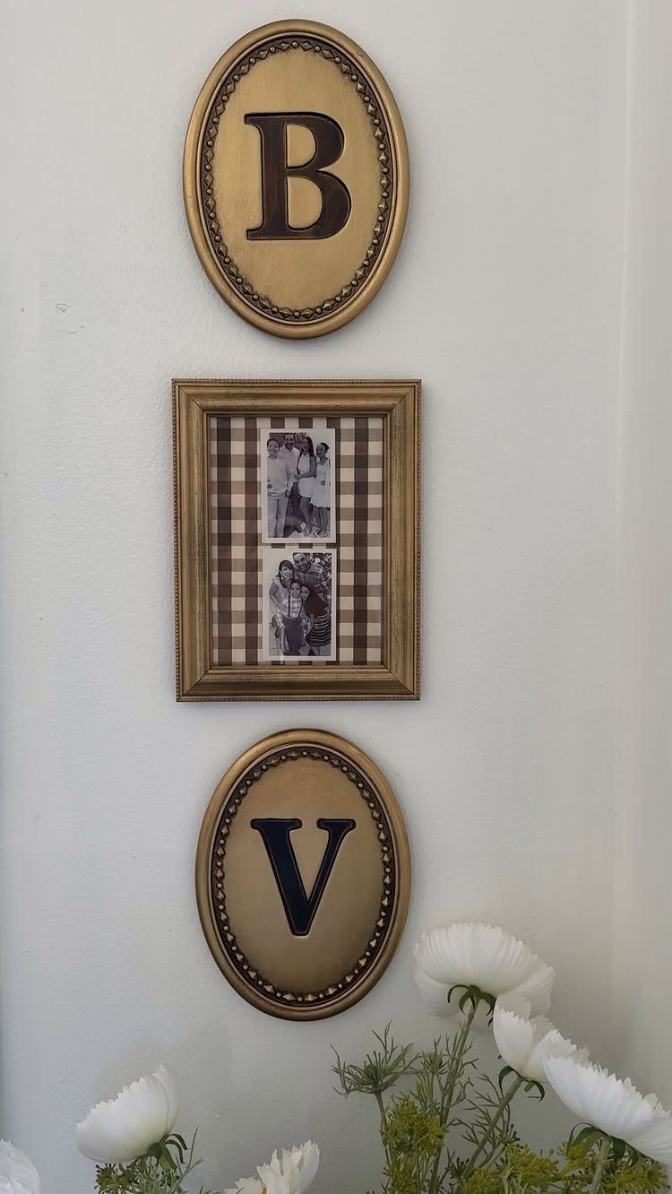 Gold oval plaques with letters B and V arranged vertically around a framed photograph on a white wall.