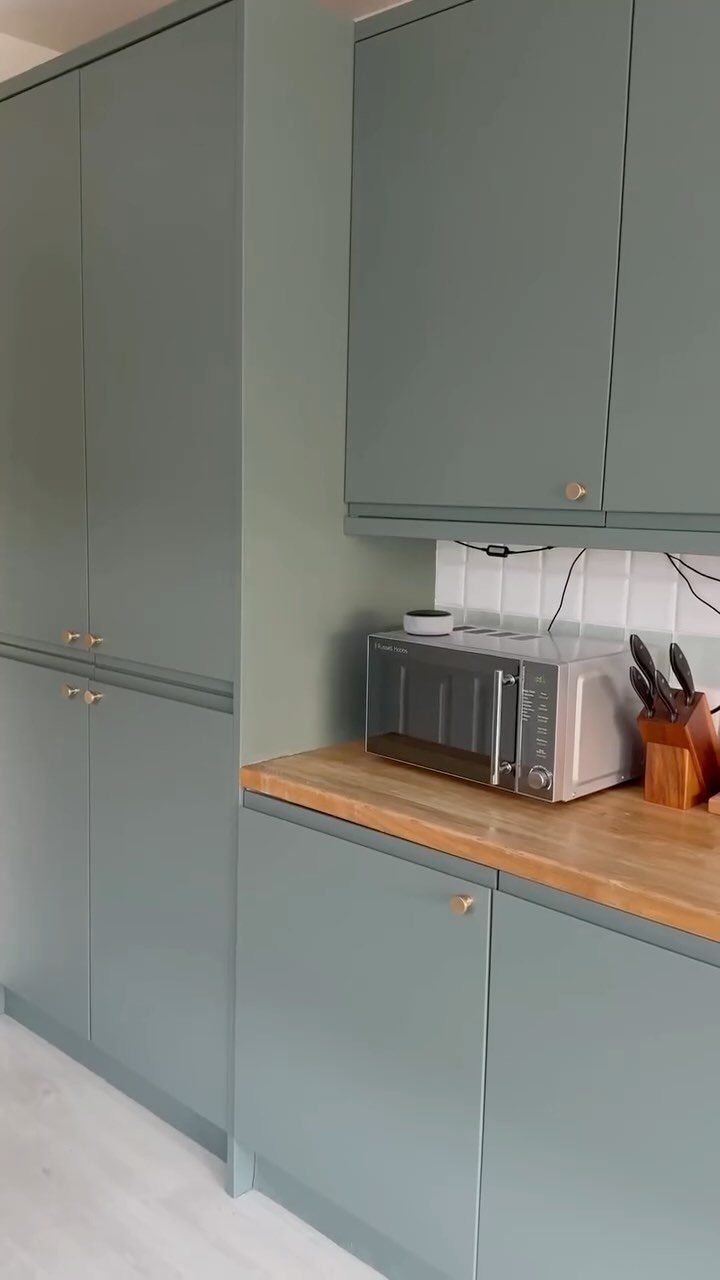 15 Kitchen Renovation Ideas for Getting the Function Back Into the Room 5 Sage green kitchen cabinets with gold handles and a wooden countertop in a bright kitchen.