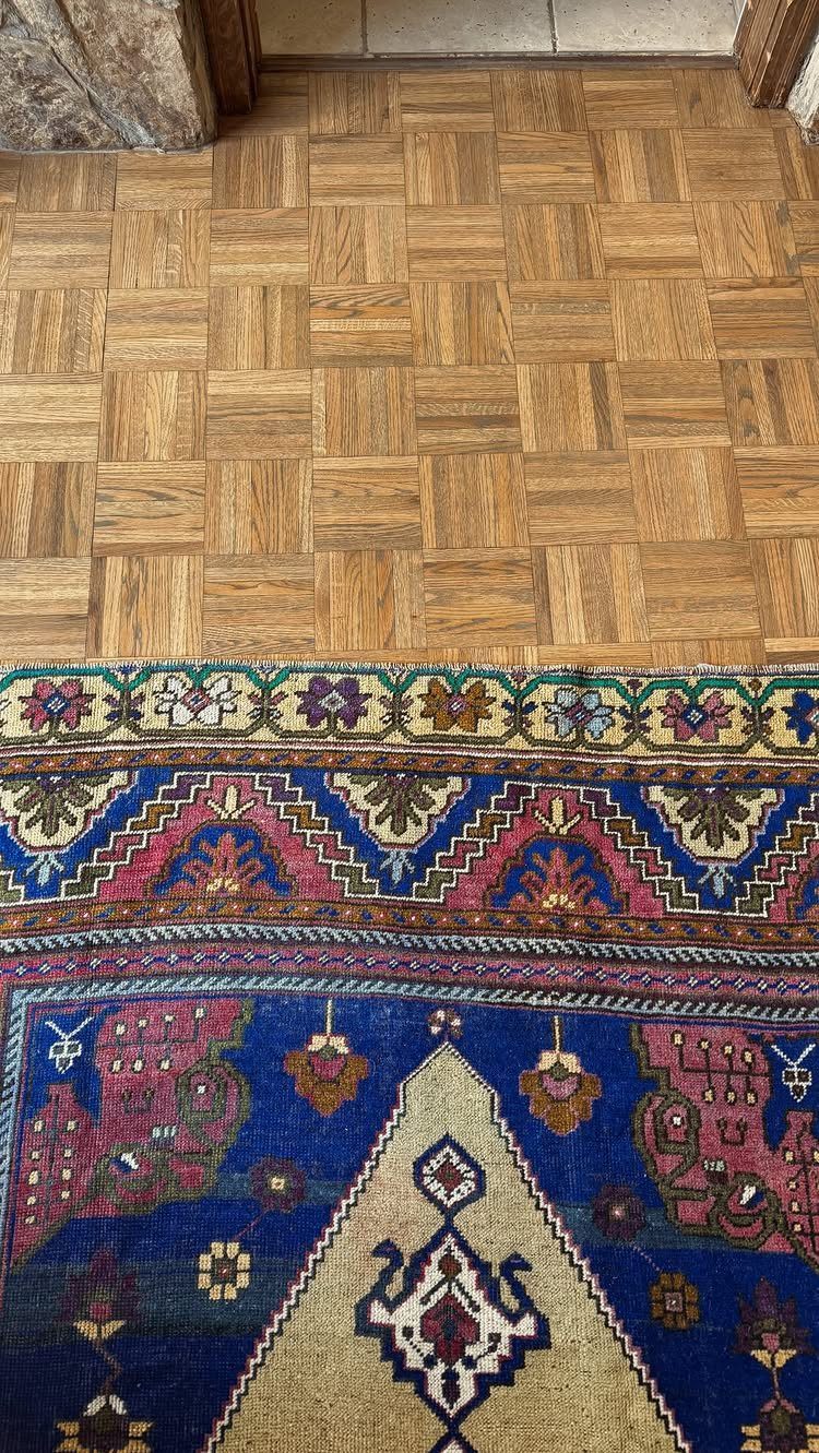 Light brown parquet wood floor with a basketweave pattern next to a colorful patterned rug.