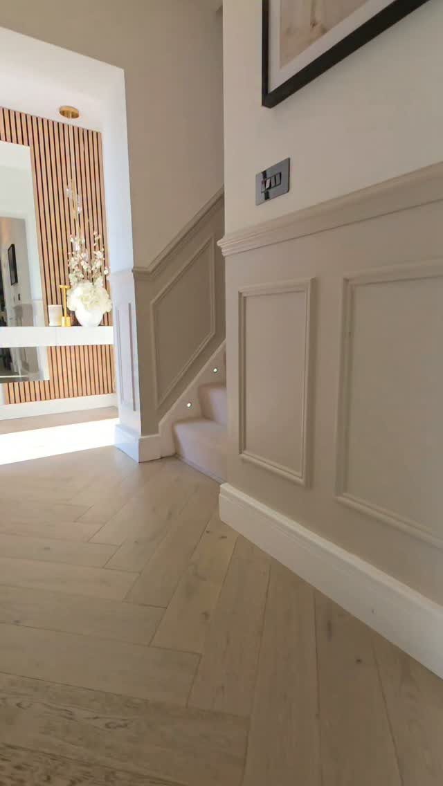 Hallway with light herringbone floors and white walls featuring decorative picture frame molding and a staircase.