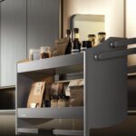 A grey tiered pull-down kitchen rack holding various jars and coffee bags inside a cabinet.