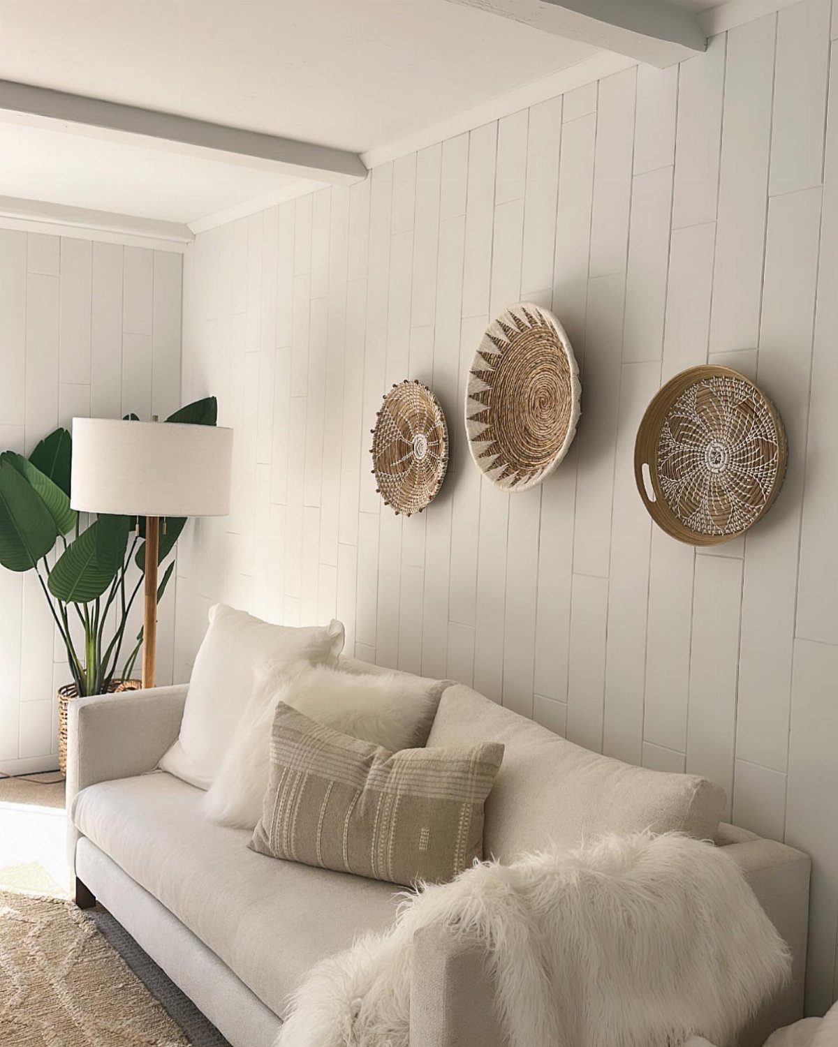 White painted wood plank wall decorated with three woven baskets above a white sofa.