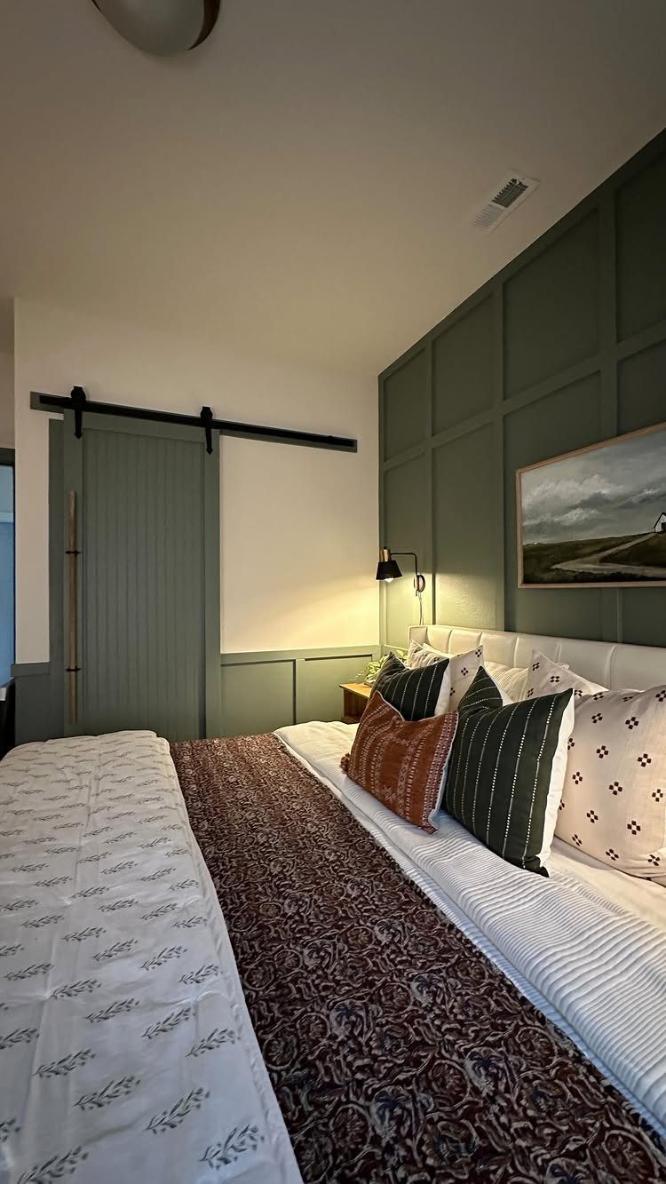 21 Bedroom Wall Decor Ideas With Photos for Every Style 13 A bed with decorative pillows sits in front of a green paneled wall and sliding barn door.
