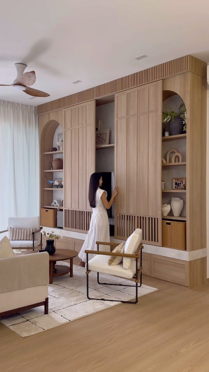 A woman interacting with large wooden sliding panels on a modern built-in wall unit.