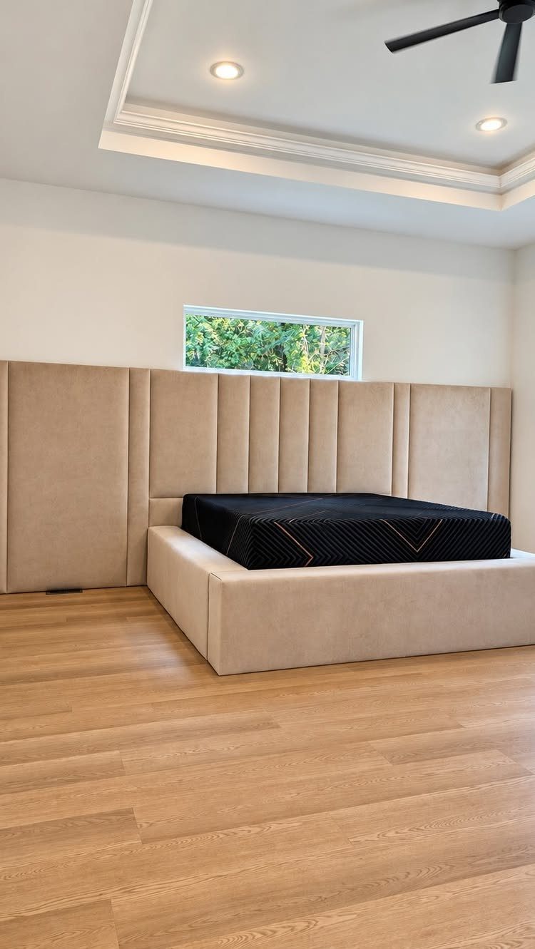20 Bedroom Wall Designs for Accent, Texture and Art 11 Beige upholstered wall panels behind a platform bed with a black mattress on wood floors.