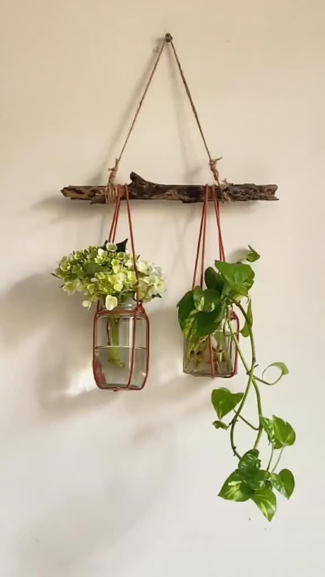 21 Bedroom Wall Decor Ideas With Photos for Every Style 10 Two glass jars with flowers and trailing greenery hanging from a rustic wooden branch.