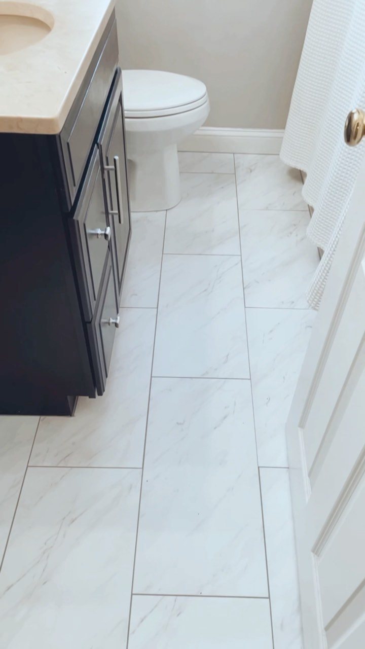 White marble-patterned rectangular tiles covering a bathroom floor next to a dark vanity.