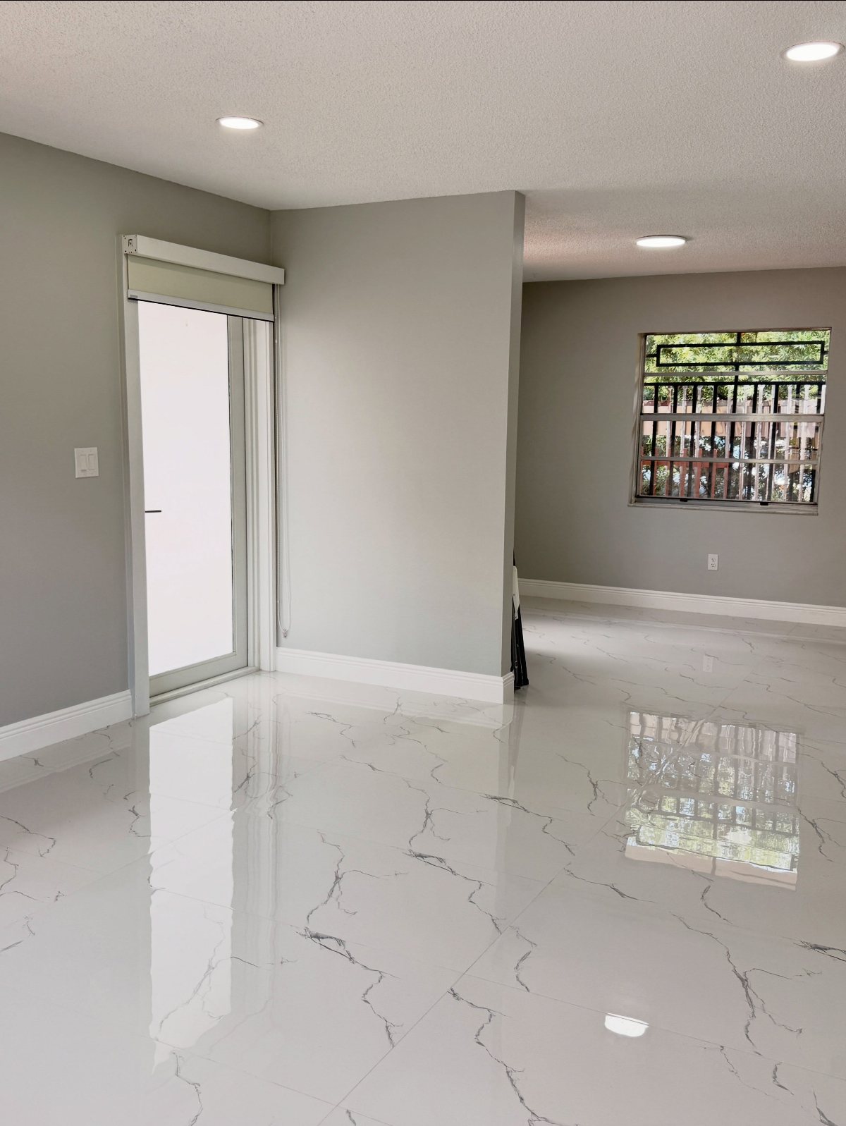 White marble-patterned tile flooring in a bright, modern room with grey walls and sliding glass doors.