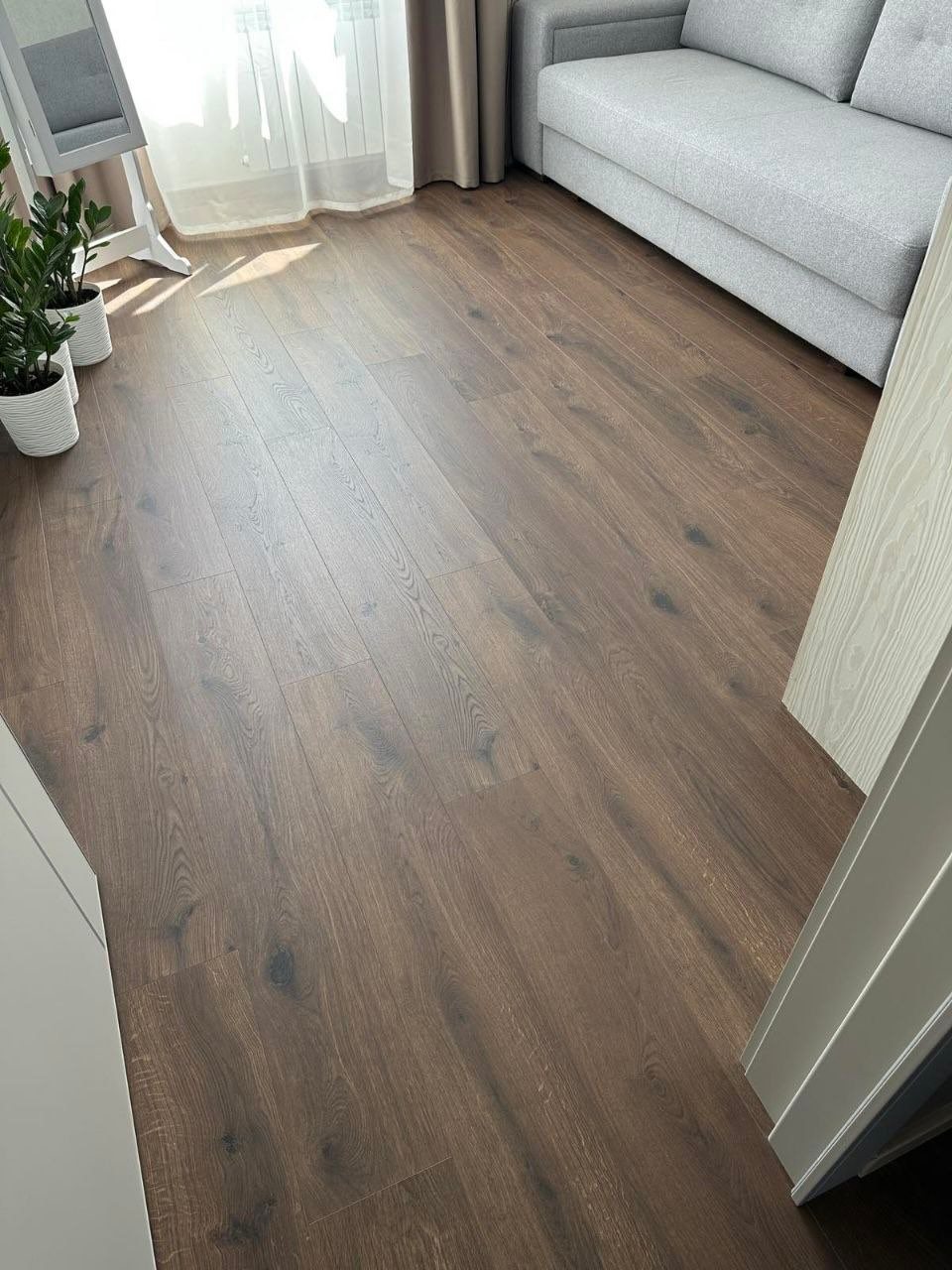 Dark brown wood-textured vinyl flooring planks in a bright, modern living room setting.