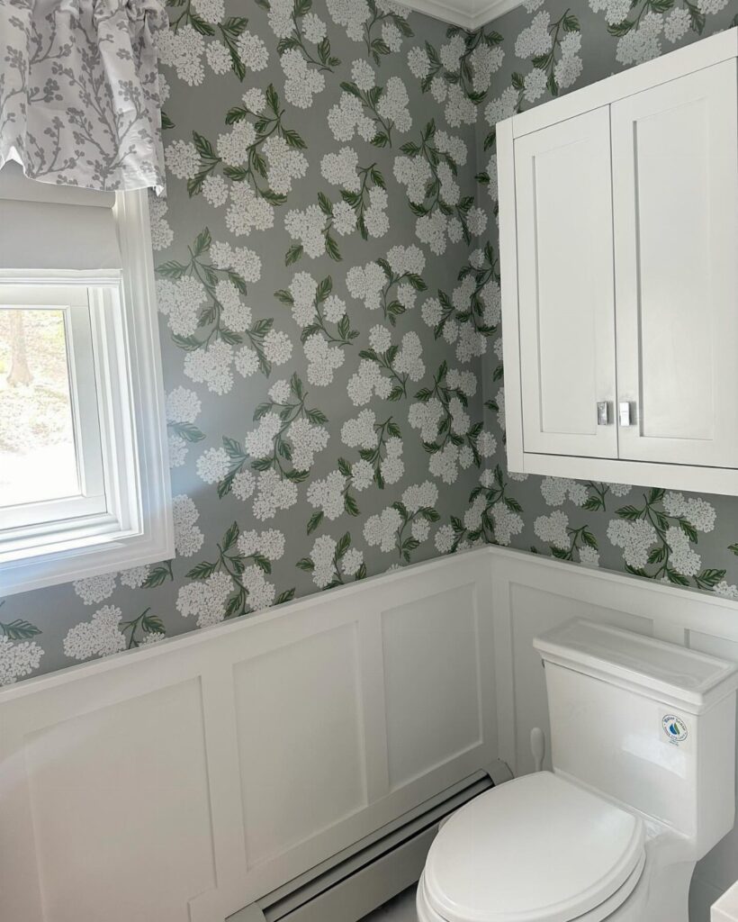 White wainscotting panels installed on a bathroom wall beneath grey floral patterned wallpaper.