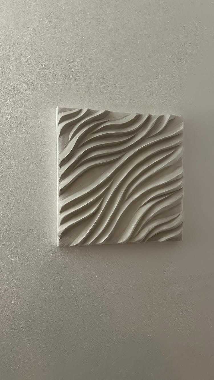 20 Bedroom Wall Designs for Accent, Texture and Art 15 A white square sculpture with wavy, three-dimensional patterns mounted on a plain wall.