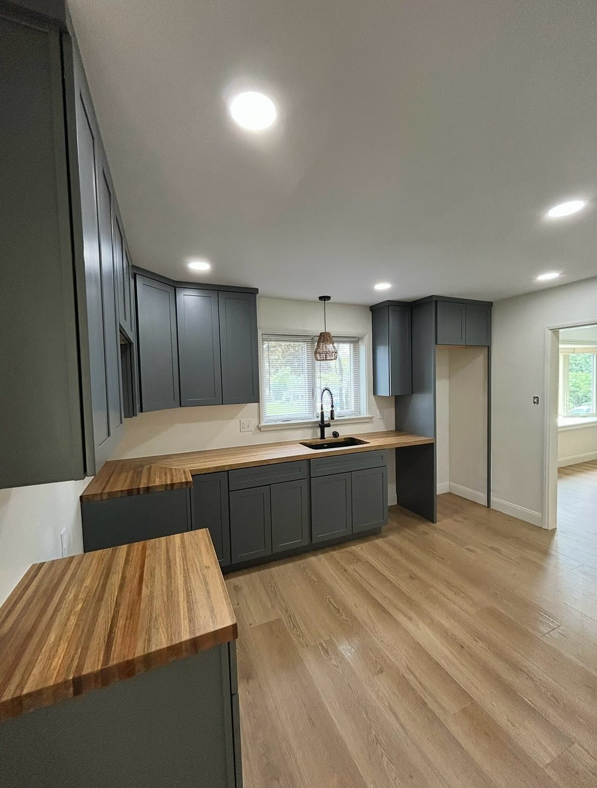 15 Kitchen Renovation Ideas for Getting the Function Back Into the Room 12 Modern kitchen with dark grey cabinetry, wooden butcher block countertops, and light wood flooring.