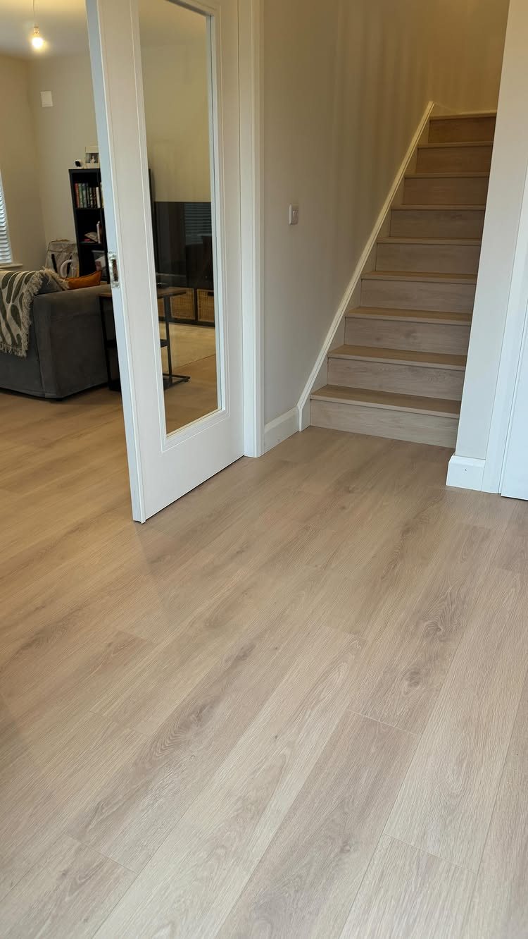 Light wood-effect laminate flooring in a hallway leading to a staircase and a white door.