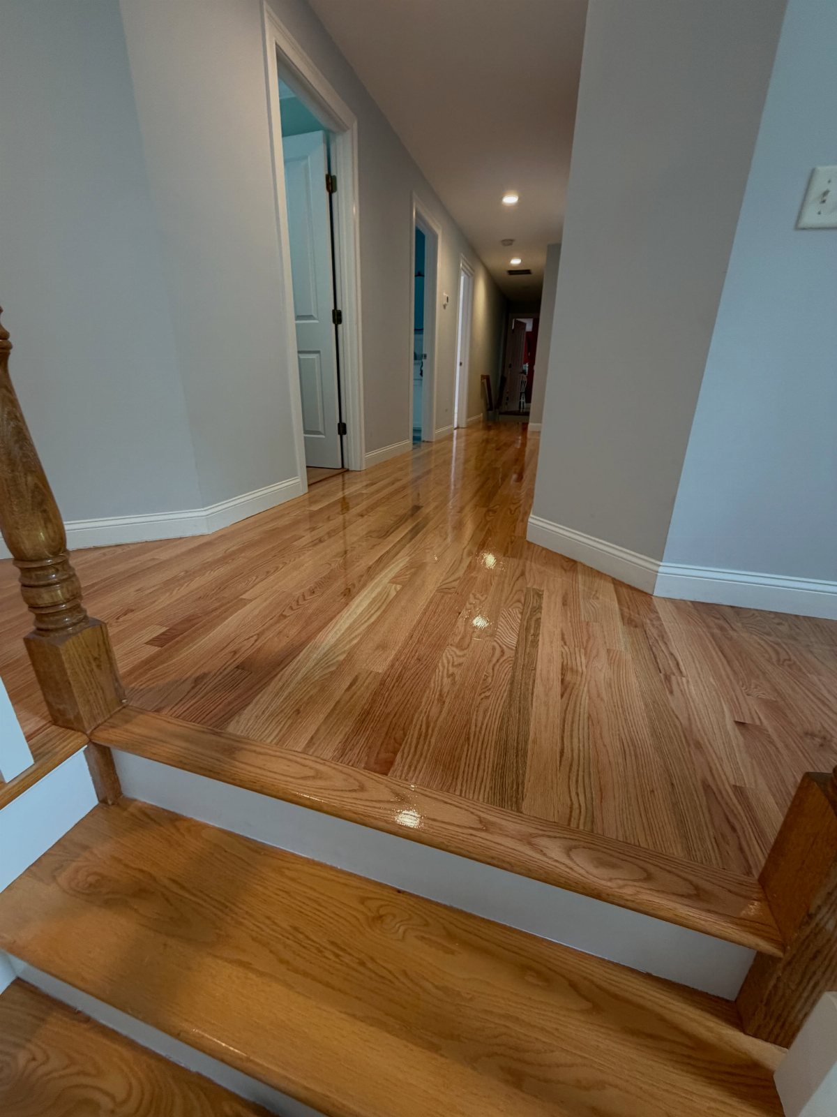 Polished warm natural oak flooring extending through a hallway and across a landing with white baseboards.