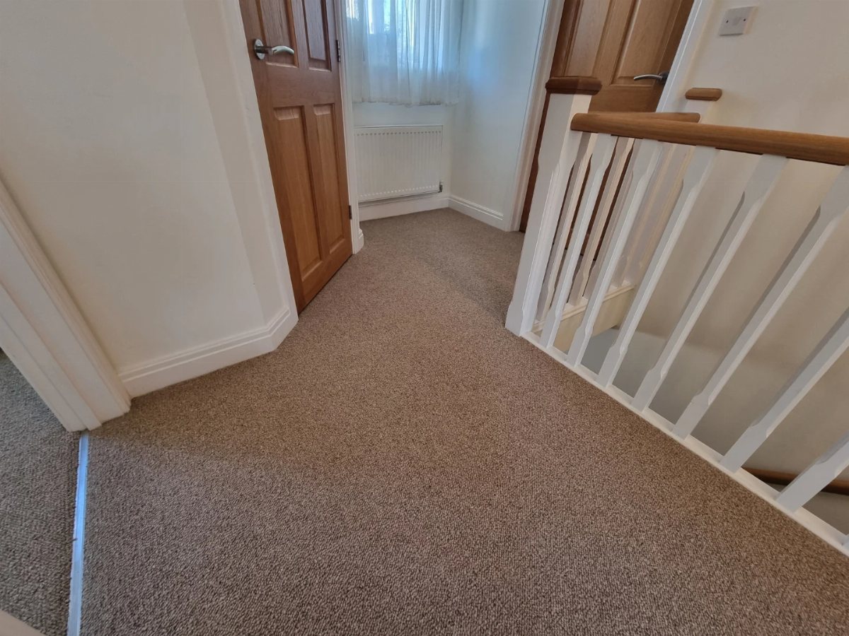 Beige oatmeal carpet installed on a hallway floor next to a wooden door and white banister.