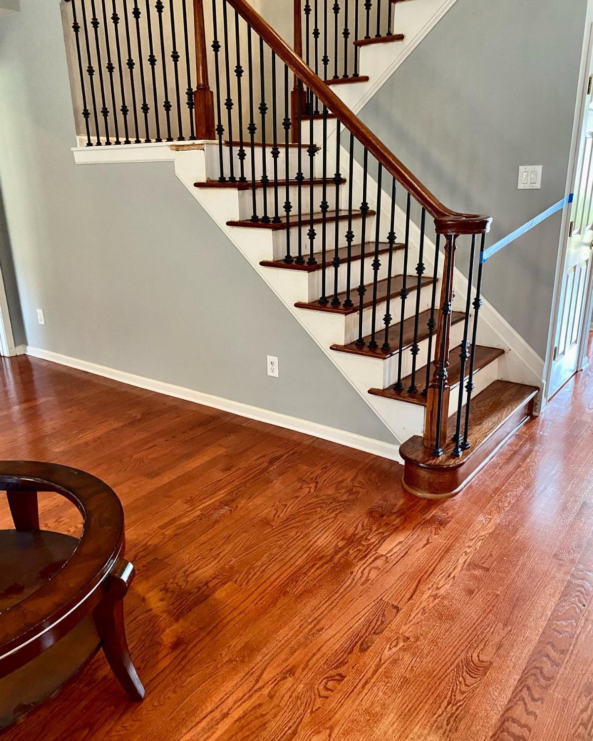 Reddish-brown hardwood flooring extends across a room next to a white and wood staircase.