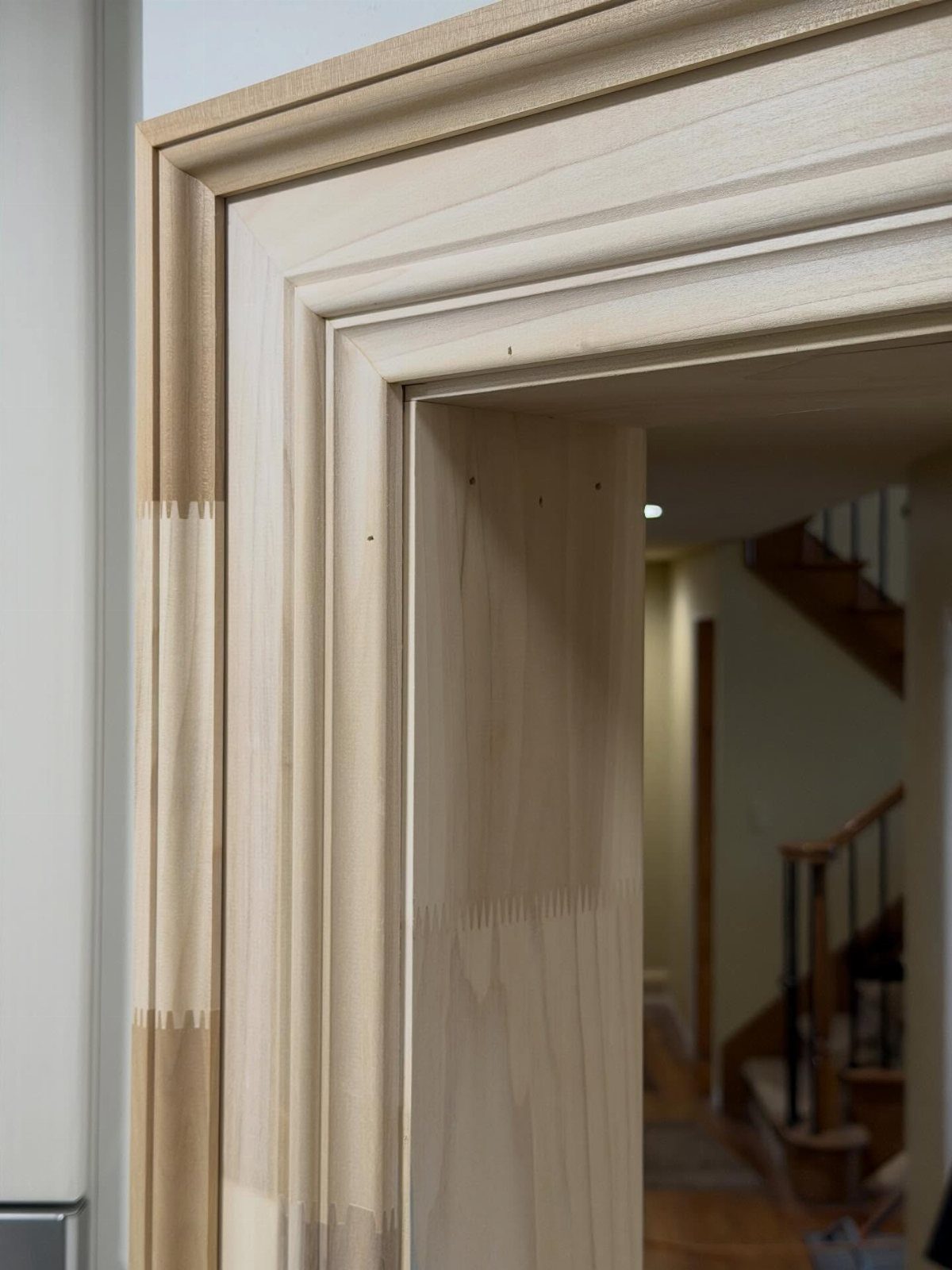 Light-colored unfinished wood door casing with decorative profiles installed around a doorway frame.