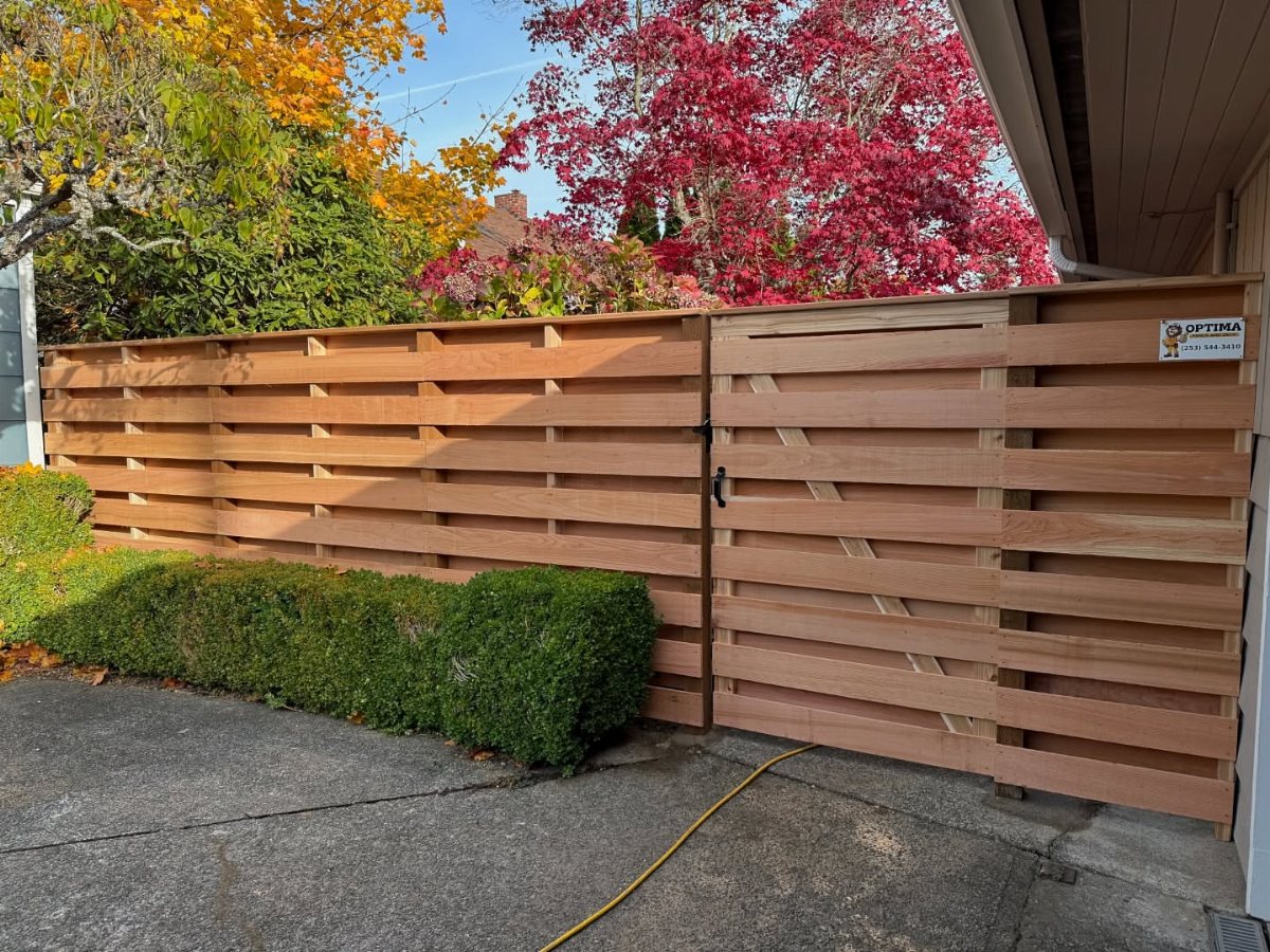 5 Wood Fence Horizontal Ideas for Every Yard 4 Horizontal cedar wood fence with slats and a gate in front of autumn trees.